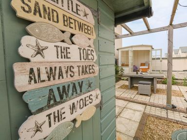 A garden area with a wooden sign on a shed and a small outdoor dining table with chairs near a summerhouse at Pebbles Reach in Fortuneswell