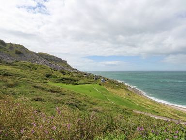 A coastal landscape with green hills rocky slopes small buildings and ocean at Pebbles Reach in Fortuneswell