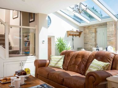 A living area with a brown leather sofa and green patterned cushions natural light from a glass ceiling wooden table with cups and snacks East Leaze Chipping Campden
