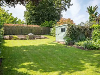A garden with a shed on the right side and a bench with a covered object near the back fence at East Leaze in Chipping Campden