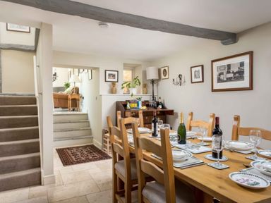 A dining room with a wooden table set for a meal and a small staircase leading to a sitting area at East Leaze in Chipping Campden