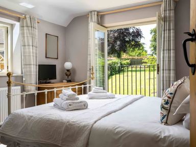 A bedroom with a bed towels on it a dresser with a television a lamp and an open door leading to a garden at East Leaze in Chipping Campden