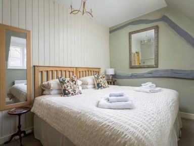 A bedroom with a double bed white bedspread floral pillows folded towels wooden headboard mirror and bedside table at East Leaze in Chipping Campden