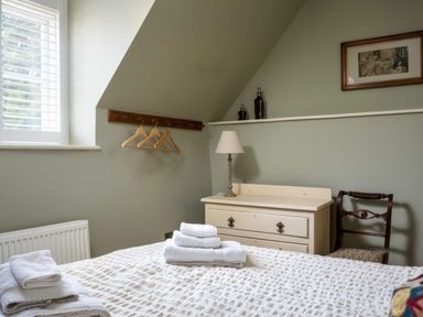 A bedroom with a bed with towels on it a chest of drawers with a lamp a chair and hangers on a wall at East Leaze in Chipping Campden