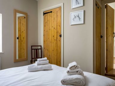A bedroom with a bed and folded towels on it two wooden doors a wooden chair and a mirror on the wall at East Leaze in Chipping Campden