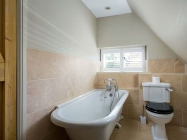 A bathroom with a bathtub and a toilet under a window at East Leaze in Chipping Campden