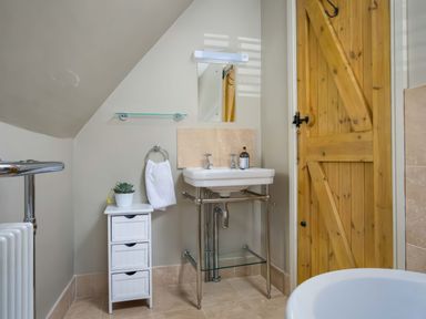 A bathroom with a wooden door a white sink a small cabinet with a plant and a towel on a holder at East Leaze in Chipping Campden