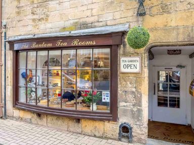 The exterior of The Bantam Tea Rooms with cakes displayed in the window and a tea garden open sign at East Leaze in Chipping Campden