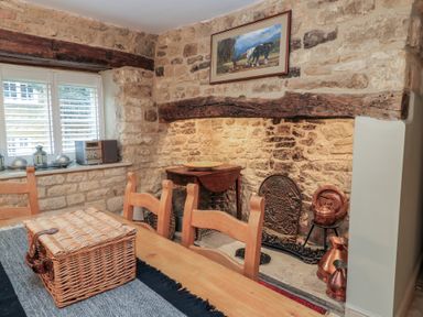 A dining room with a wooden table and chairs a wicker basket on the table exposed stone walls and a fireplace at East Leaze in Chipping Campden