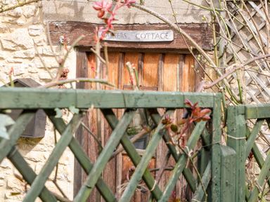 A wooden door behind a green lattice fence with plants and a stone wall at Carters Cottage in Stow on the Wold