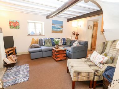A living room with a sectional sofa a striped armchair and ottoman a wooden chest coffee table and paintings on the wall at Carters Cottage in Stow-on-the-Wold