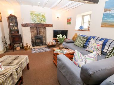 A living room with a fireplace a sofa with cushions a wooden coffee table and a TV at Carters Cottage in Stow-on-the-Wold