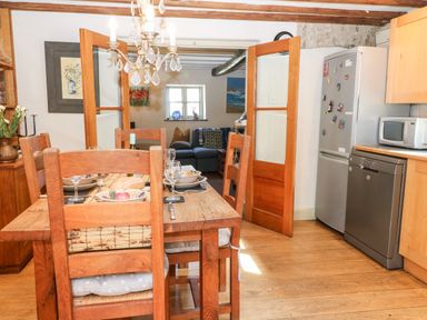 A dining area with a wooden table and chairs set for a meal next to a kitchen with a refrigerator dishwasher and microwave visible at Carters Cottage in Stow-on-the-Wold