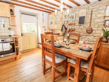 A kitchen with wooden dining table and chairs set for four near stone wall at Carters Cottage in Stow-on-the-Wold