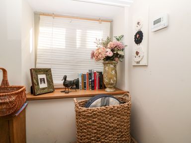A window ledge with a vase of flowers picture frame decorative duck figurine and books above a wicker basket with items in a room at Carters Cottage in Stow-on-the-Wold