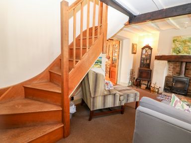 A sitting room with wooden stairs a fireplace and upholstered chairs at Carters Cottage in Stow on the Wold