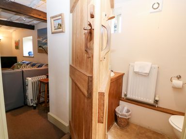 A view of a living room with couch and heater and a small bathroom with toilet and towel at Carters Cottage in Stow-on-the-Wold