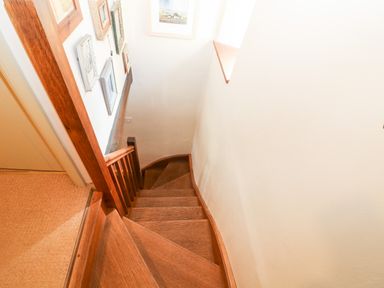 A staircase with wooden steps and handrail next to a white wall with picture frames at Carters Cottage in Stow-on-the-Wold