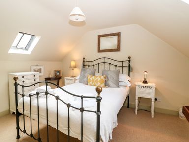 A bedroom with a black metal bed frame bedside tables lamps a chest of drawers and a skylight window at Carters Cottage in Stow on the Wold