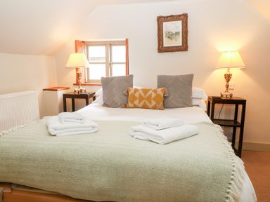 A bedroom with a bed with pillows and folded towels bedside tables with lamps and a small window at Carters Cottage in Stow-on-the-Wold