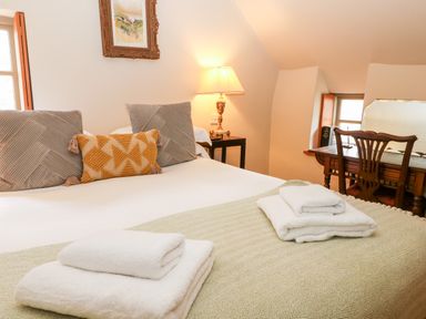 A bedroom with a made bed and folded towels a bedside lamp and a wooden desk with a chair at Carters Cottage in Stow-on-the-Wold