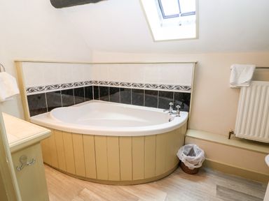 A bathroom with a corner bathtub under a skylight and a radiator with towels at Carters Cottage in Stow-on-the-Wold