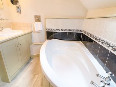 A bathroom with a white bathtub and a sink with a cabinet at Carters Cottage in Stow-on-the-Wold