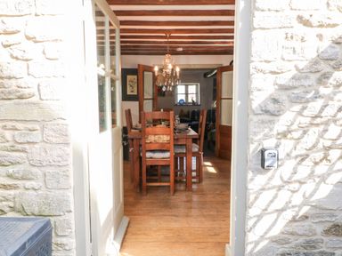 A dining room with wooden chairs and table with chandelier visible through open door at Carters Cottage in Stow-on-the-Wold