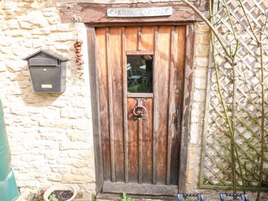 A wooden door with a window and iron handle set in a stone wall with a mailbox and trellis at Carters Cottage Stow-on-the-Wold
