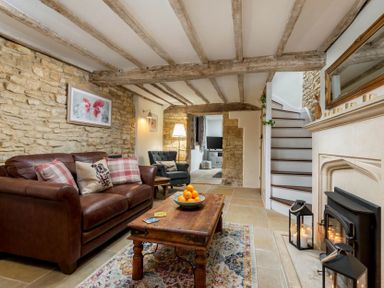 A living room with a brown leather sofa a wooden coffee table a patterned rug stone walls exposed wooden beams and a fireplace at Eastnor in Moreton-in-Marsh