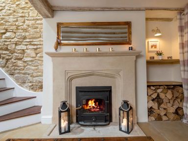A fireplace with a fire burning two lanterns with candles and a mirror above it at Eastnor Moreton-in-Marsh
