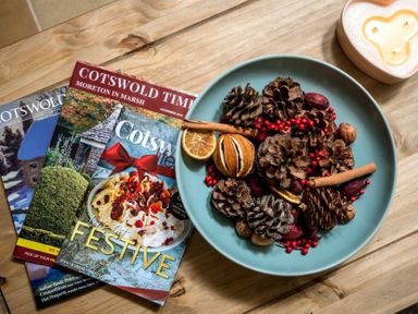 A wooden table with magazines pine cones dried fruits cinnamon sticks and a candle at Eastnor in Moreton-in-Marsh