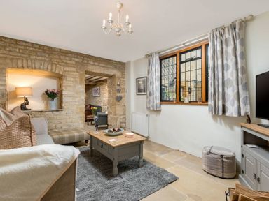 A sitting room with stone walls a wooden coffee table a sofa and a window with patterned curtains at Eastnor in Moreton-in-Marsh
