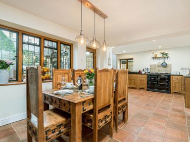 A kitchen with wooden dining table and chairs near windows and a stove at Eastnor in Moreton-in-Marsh
