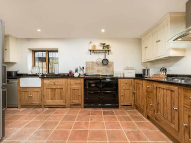 A kitchen with wooden cabinets a black oven a white sink and tiled floor at Eastnor in Moreton-in-Marsh