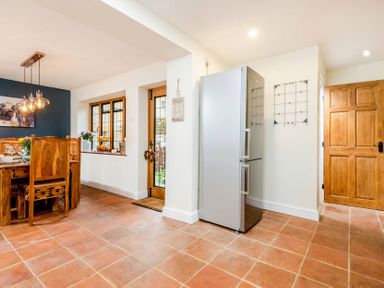 A kitchen area with a silver refrigerator wooden dining table and chairs a wooden door and windows at Eastnor in Moreton-in-Marsh