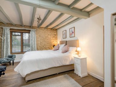 A bedroom with a bed a nightstand and window with curtains at Eastnor in Moreton-in-Marsh