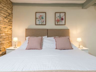 A bedroom with a bed with two pink pillows and two lamps on bedside tables at Eastnor in Moreton-in-Marsh