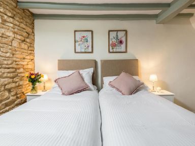 A bedroom with two single beds two bedside tables with lamps and flowers two framed floral pictures on the wall at Eastnor in Moreton-in-Marsh