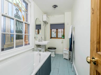 A bathroom with a bathtub under a stained glass window a sink a toilet and a small cabinet at Eastnor in Moreton-in-Marsh