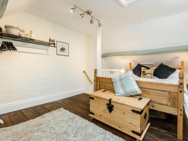 A bedroom with a wooden bed and chest next to a white wall with a hanging shelf and framed picture at Eastnor in Moreton-in-Marsh