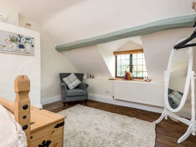A room with a gray armchair by a window wooden chest a white standing mirror and a cream rug at Eastnor in Moreton-in-Marsh