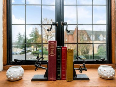 A window sill with books held by playful metal bookends and two white candle holders at Eastnor in Moreton-in-Marsh