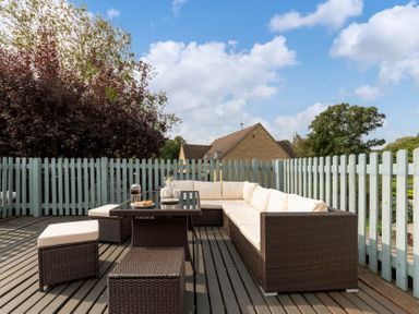 An outdoor deck with a wicker sectional sofa and table surrounded by a wooden fence at Eastnor in Moreton-in-Marsh