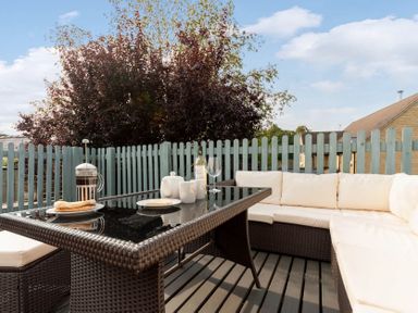 An outdoor patio with wicker furniture a glass table white cushions plates a coffee press and drinks at Eastnor in Moreton-in-Marsh