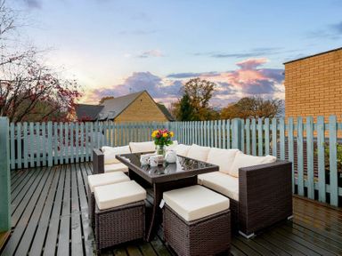 An outdoor patio with a wicker sectional sofa and table set with cushions and a vase of flowers on the table at Eastnor in Moreton-in-Marsh