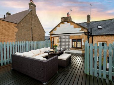 An outdoor patio with wicker furniture and cushions on a wooden deck surrounded by blue picket fences at Eastnor in Moreton-in-Marsh