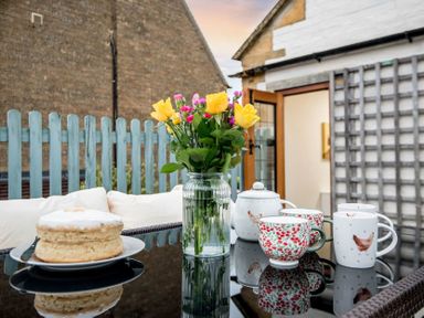 An outdoor table with a vase of yellow and pink flowers teapot cake and mugs at Eastnor in Moreton-in-Marsh