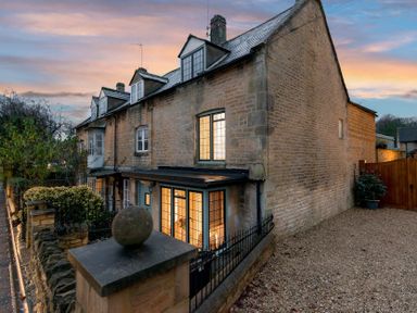 A stone house with lit windows and gravel driveway at dusk at Eastnor in Moreton-in-Marsh