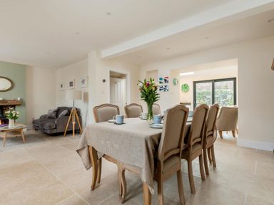 A dining area with a table and six chairs set with cups and plates next to a seating area with a sofa and coffee table at Wall Cottage in Burford